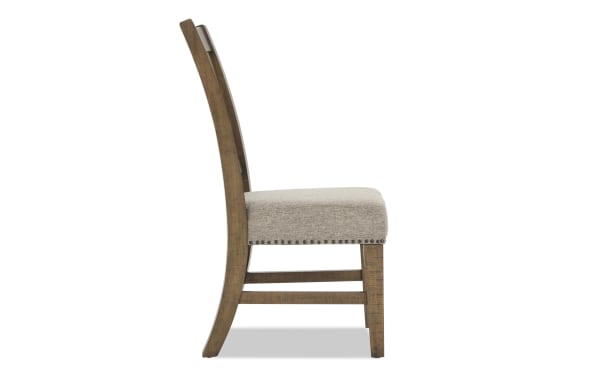 Side view of a wooden dining chair with a curved backrest and beige upholstered seat featuring nailhead trim.