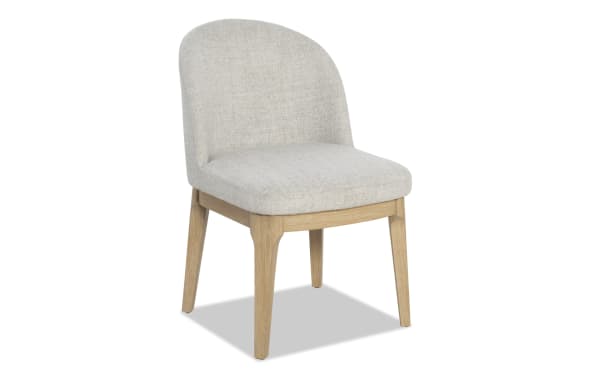 Upholstered dining chair with light beige fabric seat and backrest, supported by natural oak wooden legs, modern minimalist style.