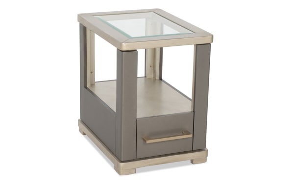 Modern end table with a glass top, gray leather panels, metal frame, and a single drawer with a metal handle, ideal for living room decor.