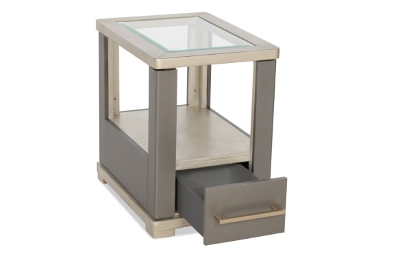 Modern side table with a glass top, gray leather panels, metal frame, and a single pull-out drawer, ideal for living room storage.