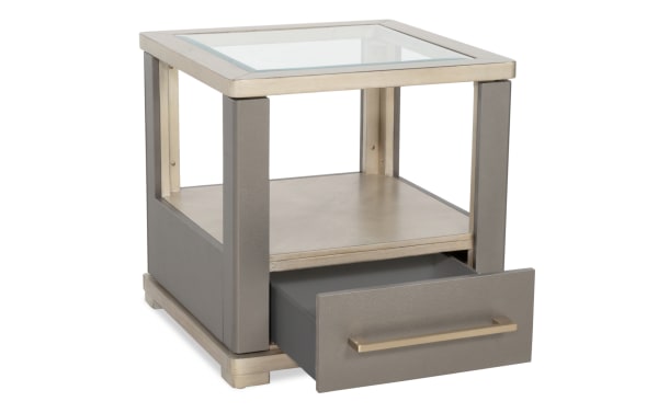 Modern square side table with a glass top, open middle shelf, and a gray leather-textured drawer with brass handle, ideal for living rooms.