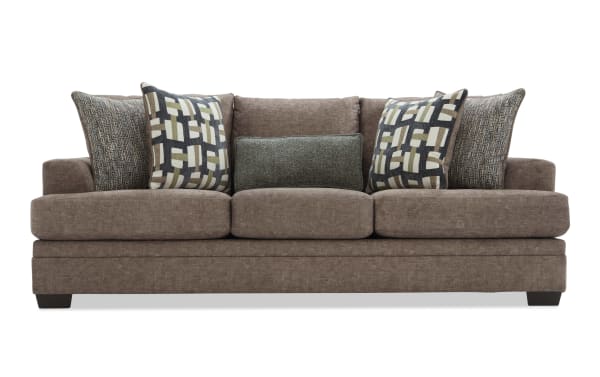 Brown fabric sofa with three large seat cushions and five decorative pillows, featuring a mix of geometric and textured patterns, modern style.