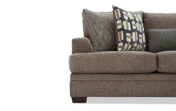 Brown fabric sectional sofa with plush cushions and three decorative pillows in geometric and textured patterns, modern living room furniture.