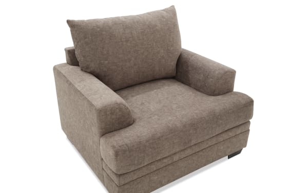 Brown upholstered fabric armchair with thick cushioned seat, backrest, and armrests, featuring a modern, boxy design and wooden legs.