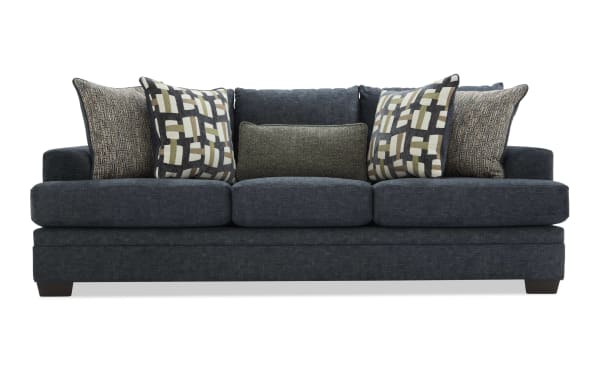 Dark blue fabric sofa with three seat cushions and six decorative pillows in geometric and textured patterns, modern living room furniture.