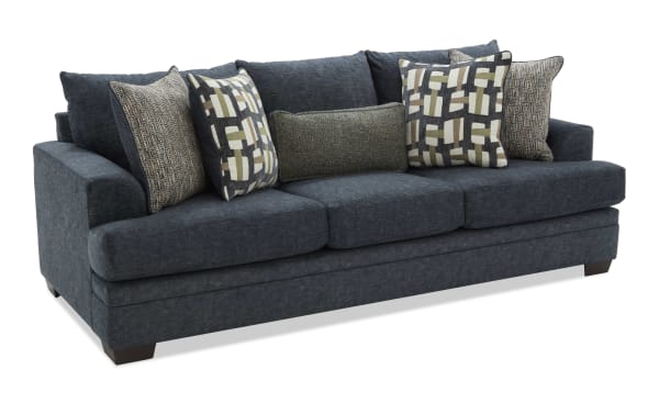 Dark blue fabric sofa with three large seat cushions, angled arms, and six decorative pillows in geometric and textured patterns, modern style.