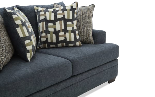 Dark blue fabric sofa with thick cushions and four decorative pillows featuring geometric and textured patterns, modern living room furniture.