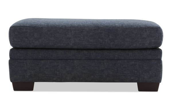 Dark blue fabric upholstered rectangular ottoman with cushioned top and wooden block legs, suitable for living room seating or footrest.