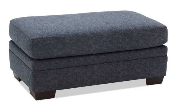 Dark blue upholstered rectangular ottoman with soft fabric, cushioned top, and short wooden legs, suitable for living room seating or footrest.