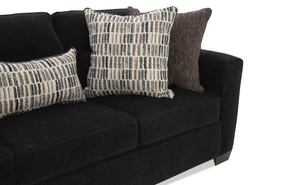 Black fabric sofa with plush cushions, featuring two patterned beige and brown throw pillows and one solid brown pillow, showcasing modern living room decor.