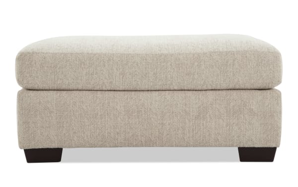Beige Cypress Ottoman upholstered in durable polyester fabric with Bob-O-Pedic® memory foam cushion, transitional style, and dark wooden legs.