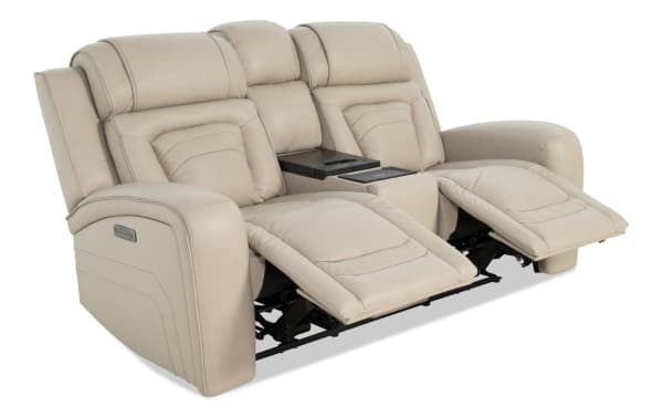 Beige leather reclining loveseat with padded armrests, adjustable footrests, and a center console with cup holders, designed for comfort and relaxation.