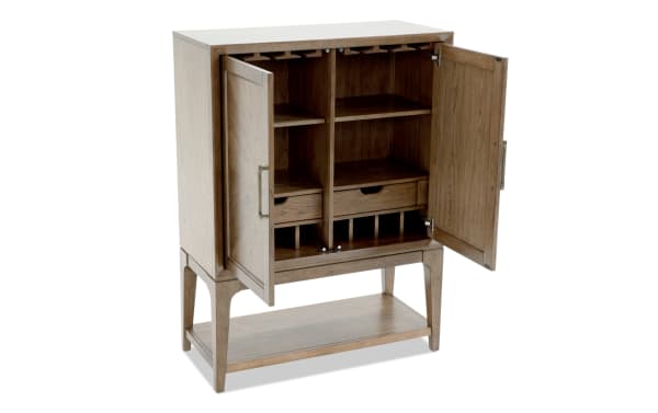 Wooden bar cabinet with open double doors, featuring multiple shelves, wine glass racks, drawers, and a lower open shelf, in a light brown finish.