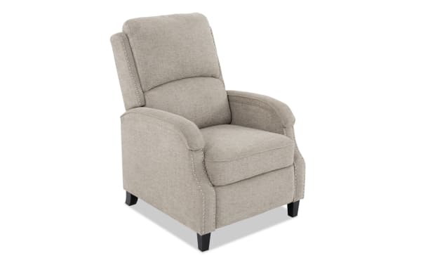 Beige fabric recliner chair with cushioned back and seat, nailhead trim accents, and dark wooden legs, suitable for living room seating.