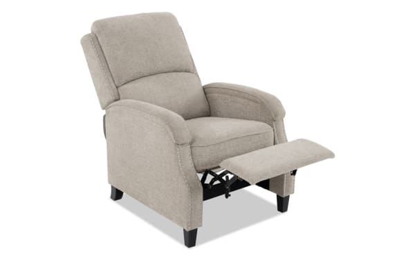 Beige fabric recliner chair with padded armrests, nailhead trim detailing, and black wooden legs, shown with footrest extended.