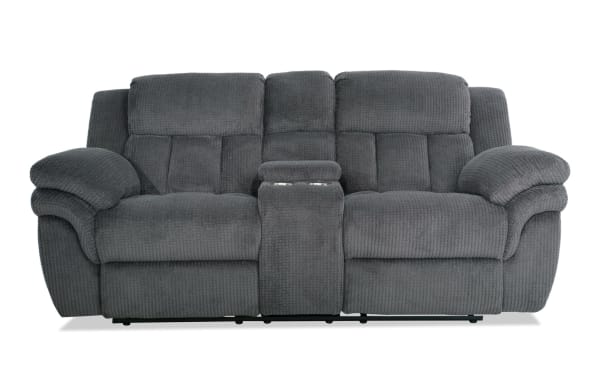 Dark gray plush fabric reclining loveseat with padded armrests, high back cushions, and a center console with cup holders, designed for comfort and relaxation.