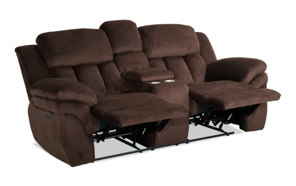 Brown plush fabric reclining loveseat with padded armrests, cushioned backrests, and a central console with cup holders, designed for comfort and relaxation.