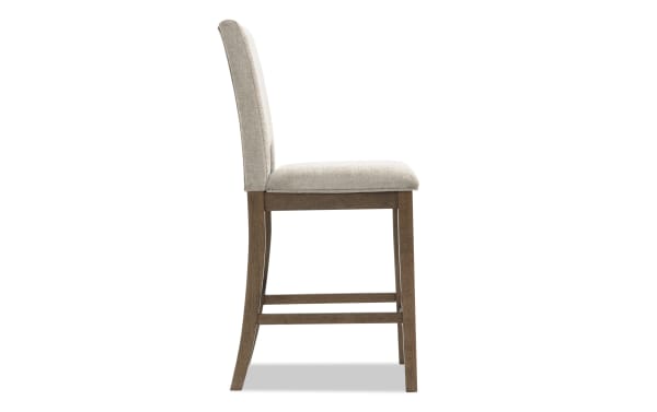 Upholstered beige fabric dining chair with cushioned seat, wooden frame and legs in a medium brown finish, side view.