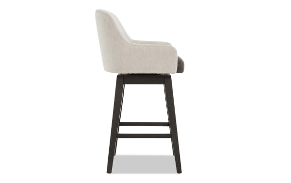 Modern bar stool with beige fabric upholstered backrest and dark brown leather seat cushion, supported by dark wood legs and footrest.