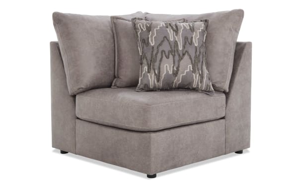 Gray corner accent chair upholstered in soft fabric with plush cushions and a patterned decorative throw pillow, ideal for modern living rooms.