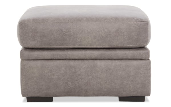 Gray leather ottoman with cushioned top and dark wooden legs, featuring a soft textured finish and modern rectangular design.