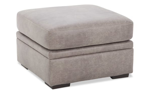 Square gray upholstered ottoman with plush cushion top and dark wooden legs, suitable for living room seating or footrest.