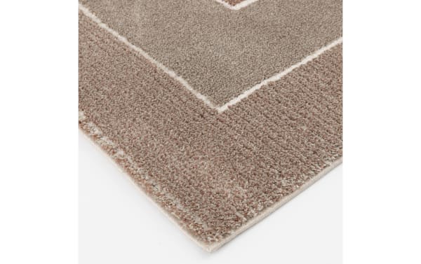 Corner close-up of the Atlas 5' x 7' Rust Geometric Rug showing thick, soft polypropylene pile in rust and muted orange tones with a bold geometric pattern.