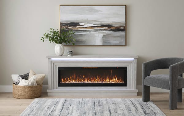 Modern electric fireplace with a light wood frame, realistic flame effect, and a gray upholstered armchair beside it, styled with a woven basket of cushions and abstract wall art.