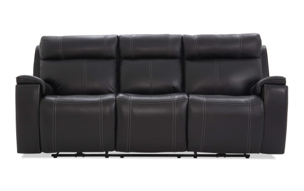 Black leather reclining sofa with three seats, featuring plush cushioning, visible white stitching, and padded armrests for living room comfort.