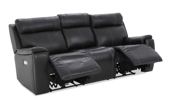 Black leather reclining sofa with three seats, visible stitching, padded armrests, and extended footrests for enhanced comfort.