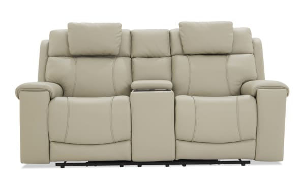 Beige leather reclining loveseat with padded armrests, adjustable headrests, and a central console for storage or cup holders, designed for comfort and style.