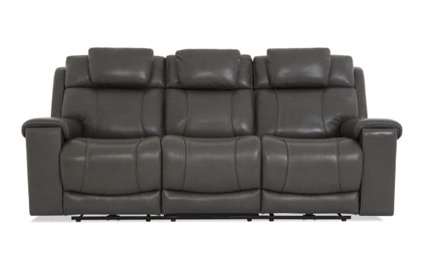 Dark gray leather reclining sofa with three seats, padded armrests, and cushioned headrests, designed for living room comfort.