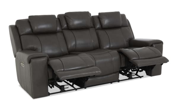 Dark gray leather reclining sofa with three seats, padded headrests, and visible manual recliner controls on armrests, designed for comfort and relaxation.