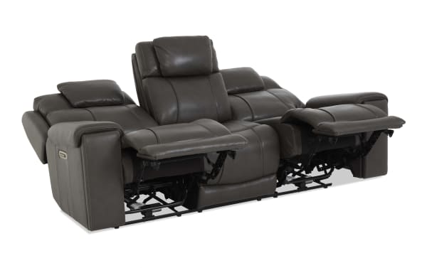 Dark gray leather reclining sofa with three seats, featuring padded armrests, headrests, and extended footrests for enhanced comfort.