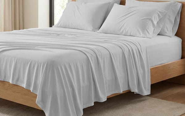 King-size bed with soft, light gray microfiber sheets and pillowcases on a wooden frame, showcasing smooth, wrinkle-resistant bedding.