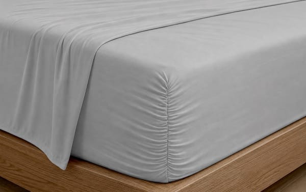 Light gray fitted sheet with elasticized corner on a wooden bed frame, showcasing smooth, wrinkle-resistant microfiber fabric for a modern bedroom.