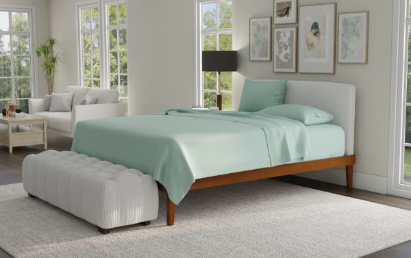 Modern bedroom with a wooden platform bed featuring a light gray upholstered headboard, mint green bedding, a tufted gray bench, and framed abstract wall art.