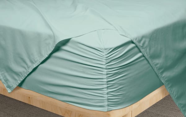 Teal fitted sheet on a wooden bed frame with gathered elastic edges, showcasing smooth, wrinkle-resistant fabric ideal for a modern bedroom.