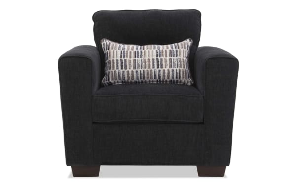 Dark gray upholstered armchair with wide padded arms, cushioned back, and a rectangular patterned lumbar pillow, featuring wooden block legs.