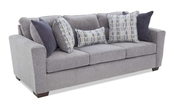 Gray fabric sofa with three seat cushions, dark wooden legs, and six decorative pillows in blue and patterned designs, modern style.