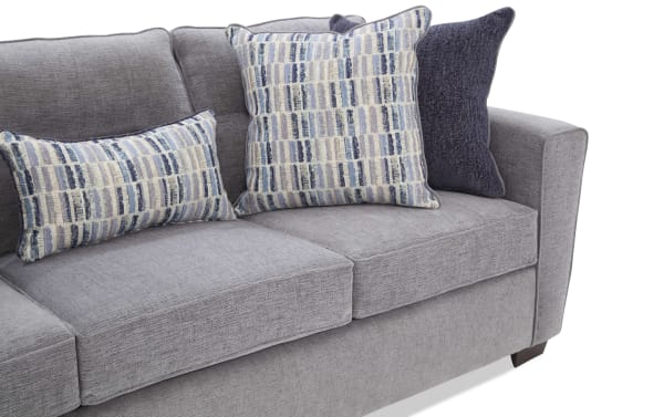 Gray fabric sofa with three decorative pillows, featuring textured upholstery and patterned cushions in blue and beige tones.