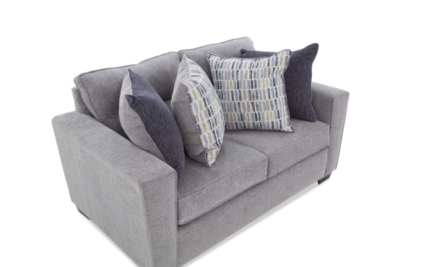 Modern gray fabric loveseat with wide armrests, two seat cushions, and four decorative throw pillows in blue and patterned designs.