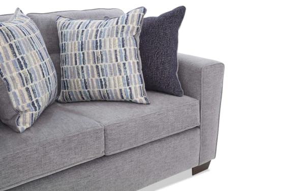 Gray fabric sofa with two patterned blue and beige throw pillows and one solid dark blue pillow, featuring clean lines and wooden legs.