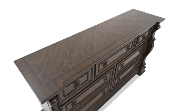 Dark wood dresser with ornate carved details, multiple drawers, and antique brass handles, showcasing classic traditional furniture style.