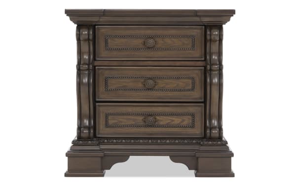 Dark brown wooden nightstand with three ornately carved drawers, decorative molding, and a classic vintage design.