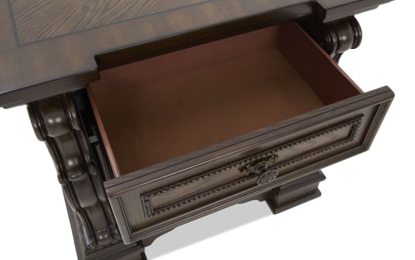 Dark wood drawer with ornate carved details and brass knob, open to show empty interior, part of classic wooden desk or table.