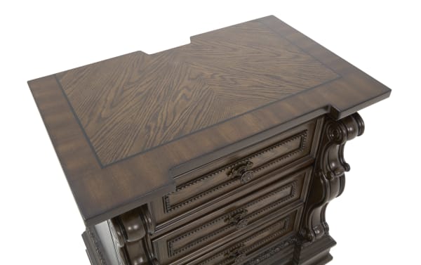 Dark brown wooden dresser top with intricate wood grain pattern and decorative trim, featuring ornate carved side details and brass drawer handles.
