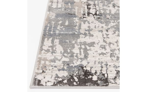 Corner view of a modern area rug with an abstract pattern in shades of gray, beige, and cream, featuring a soft, textured surface and finished edges.
