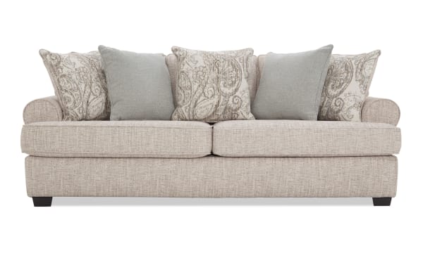 Beige fabric sofa with rolled arms, two large seat cushions, and five decorative throw pillows in paisley and solid patterns, modern style.
