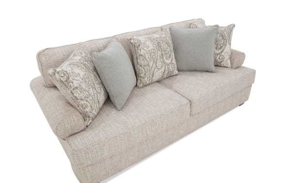 Beige fabric sofa with textured upholstery, featuring rolled arms and six decorative throw pillows in paisley and solid light gray patterns, ideal for modern living rooms.